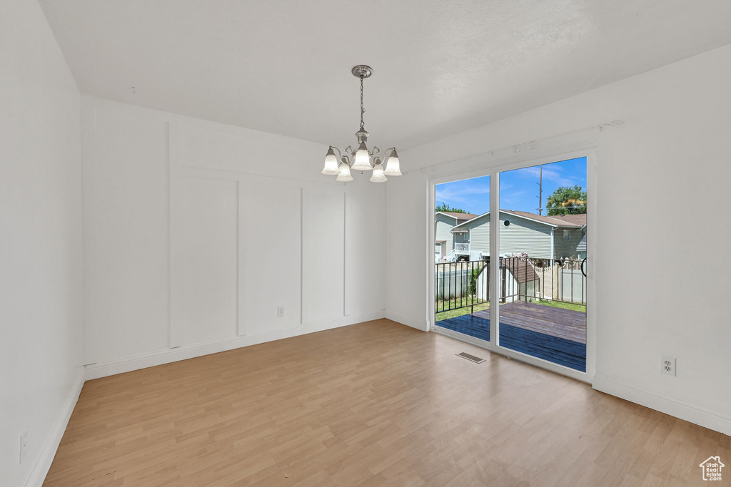 Empty room with a chandelier, light wood-style flooring, and baseboards
