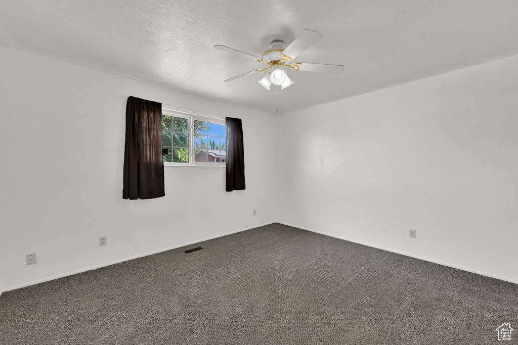 Spare room with ceiling fan, dark carpet, baseboards, and a textured ceiling