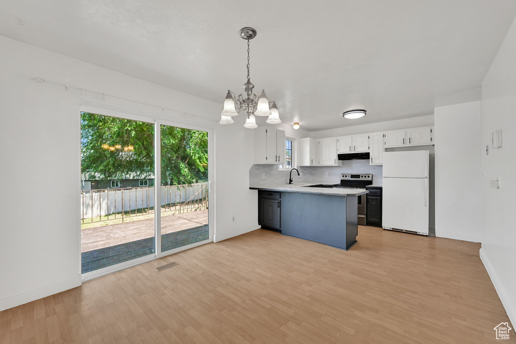 Kitchen with freestanding refrigerator, a chandelier, stainless steel range with electric stovetop, under cabinet range hood, and a peninsula
