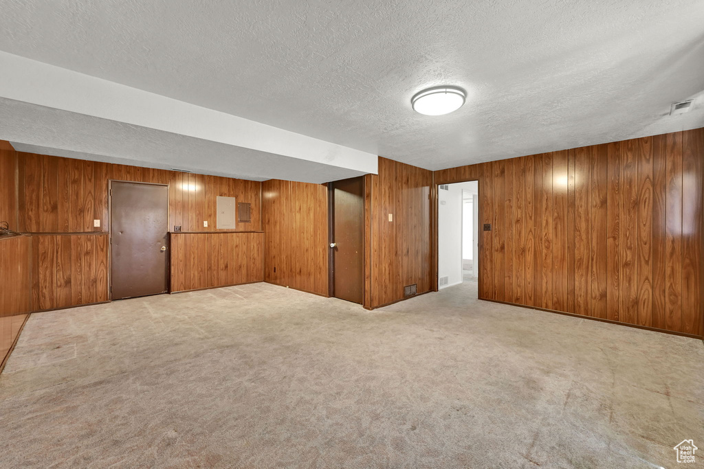 Carpeted empty room featuring a textured ceiling, wood walls, and electric panel