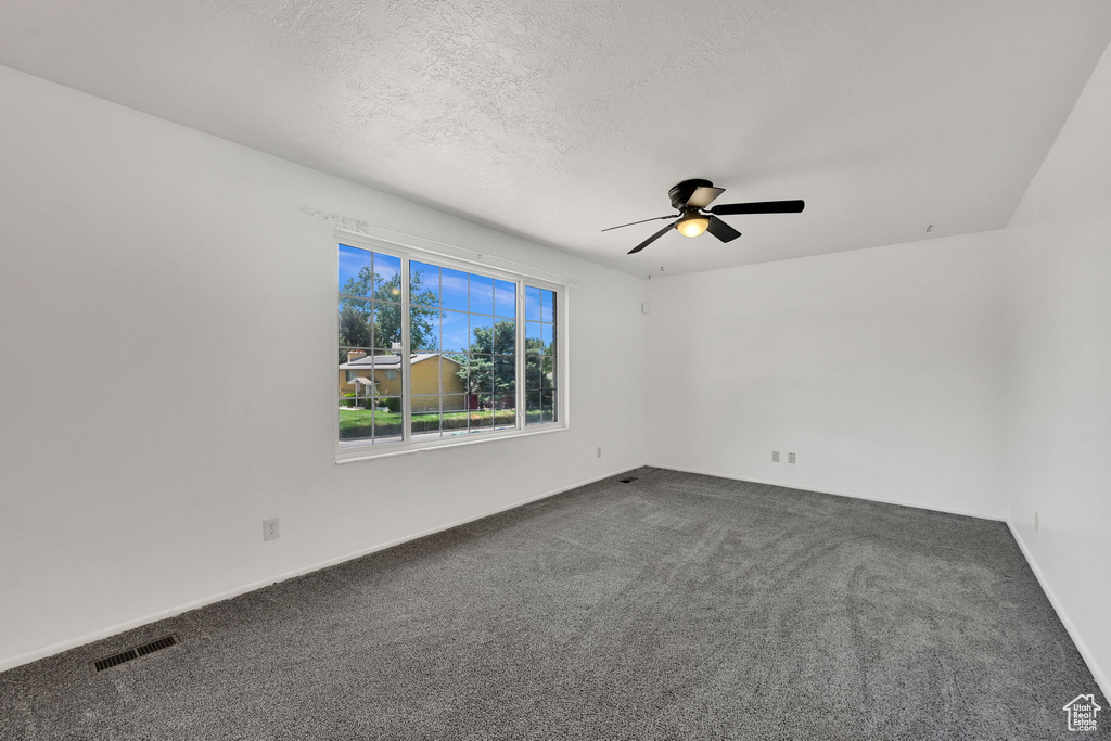 Empty room featuring a ceiling fan, dark carpet, a textured ceiling, and baseboards
