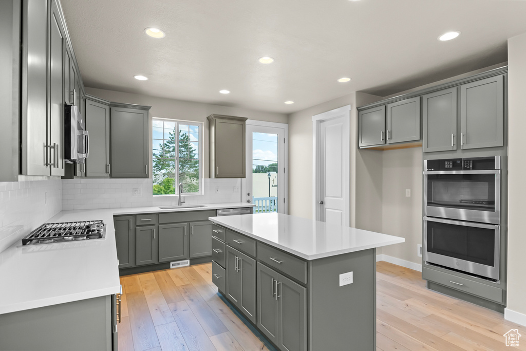 Kitchen featuring appliances with stainless steel finishes, a sink, gray cabinetry, decorative backsplash, and recessed lighting