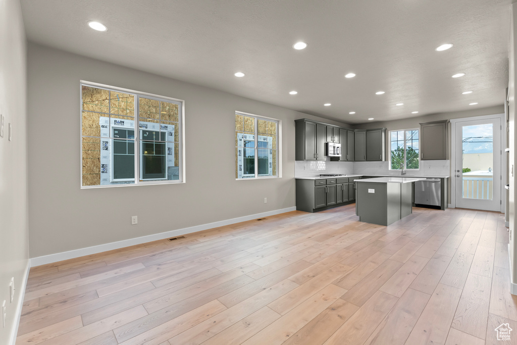 Kitchen with appliances with stainless steel finishes, a center island, recessed lighting, light wood finished floors, and gray cabinets