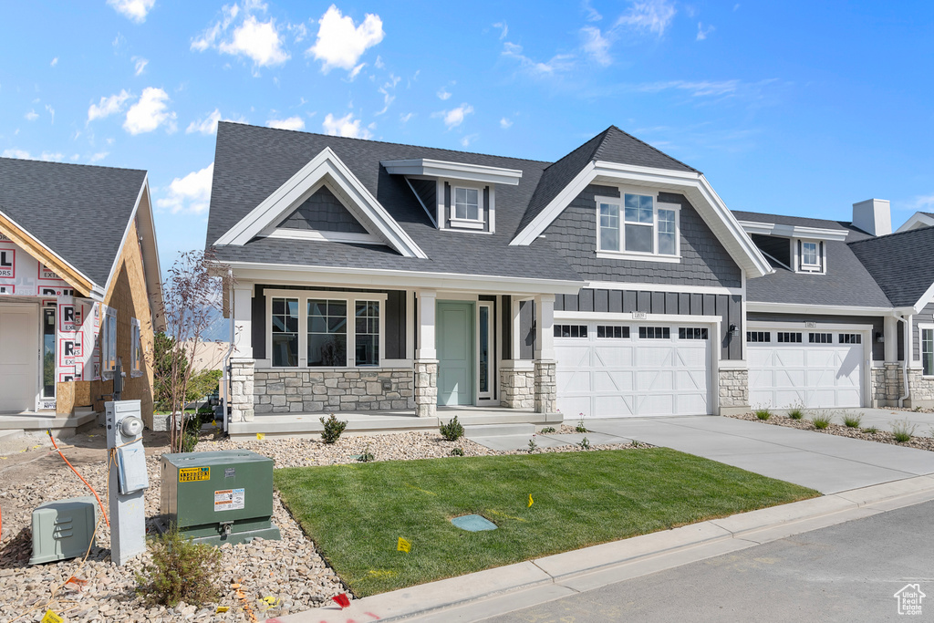 View of front facade featuring stone siding, a shingled roof, a porch, and concrete driveway