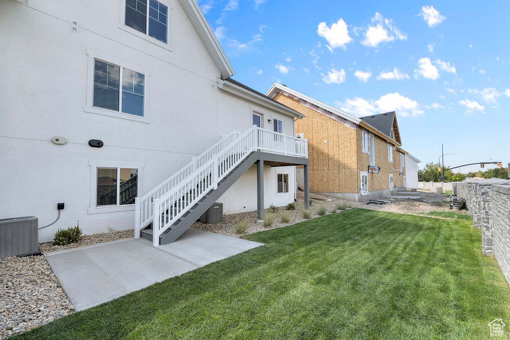 Rear view of house with stucco siding, stairway, central AC, a lawn, and a patio