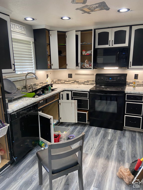 Kitchen with black appliances, open shelves, wood finished floors, a sink, and light stone countertops
