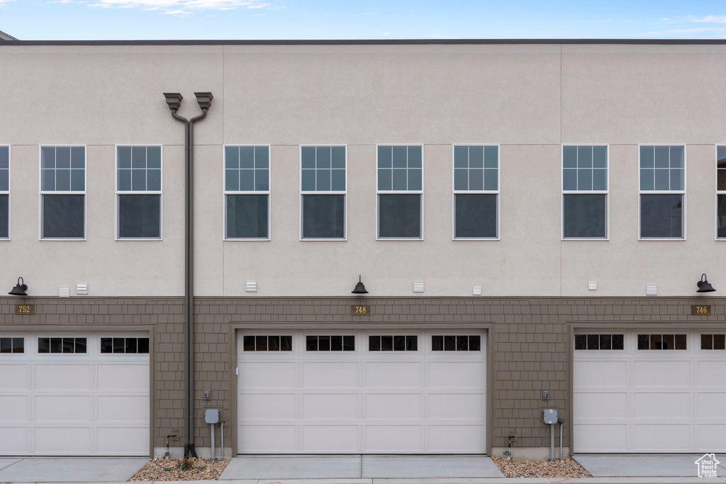 Rear view of house with stucco siding, an attached garage, and driveway