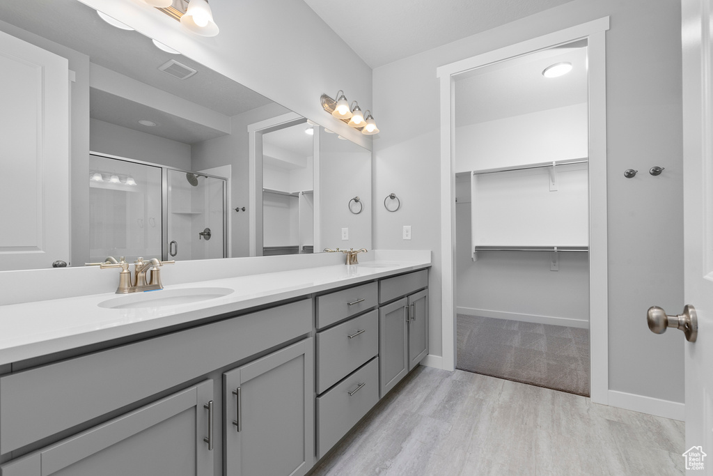 Bathroom with double vanity, a spacious closet, a stall shower, wood finished floors, and baseboards