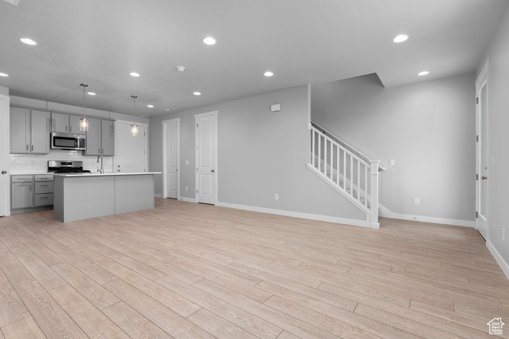 Kitchen with appliances with stainless steel finishes, gray cabinets, a sink, light wood-style floors, and recessed lighting
