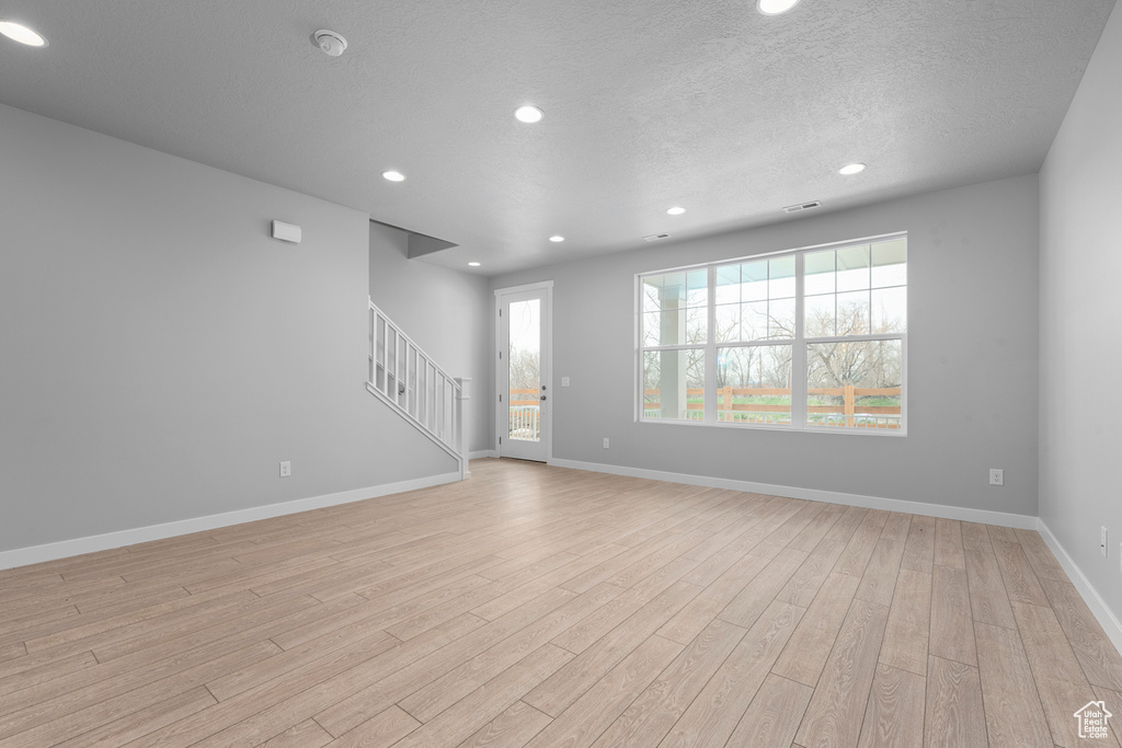 Unfurnished living room with light wood-style floors, stairs, recessed lighting, baseboards, and a textured ceiling