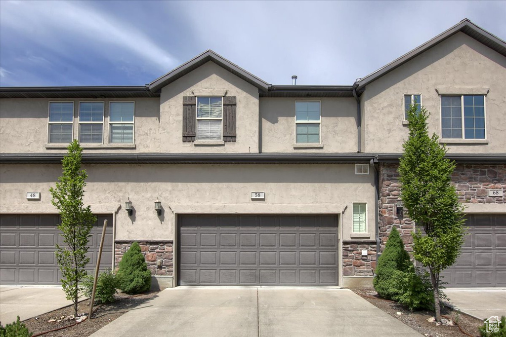 View of front facade featuring stone siding, stucco siding, and driveway