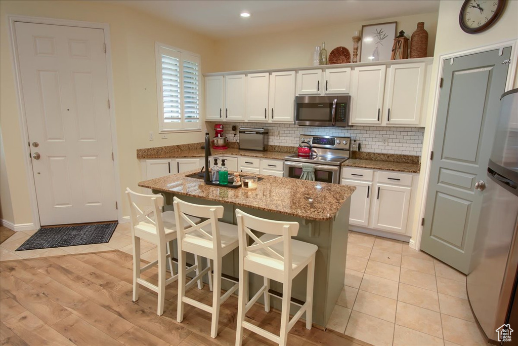 Kitchen with appliances with stainless steel finishes, white cabinetry, backsplash, light stone counters, and recessed lighting
