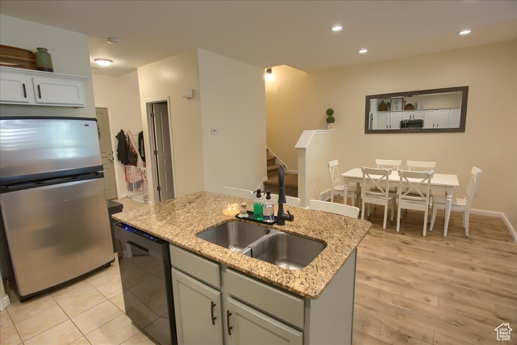 Kitchen featuring freestanding refrigerator, dishwasher, a sink, a kitchen island with sink, and light stone countertops