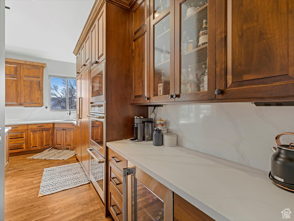 Kitchen with beverage cooler, light wood finished floors, a sink, and glass insert cabinets