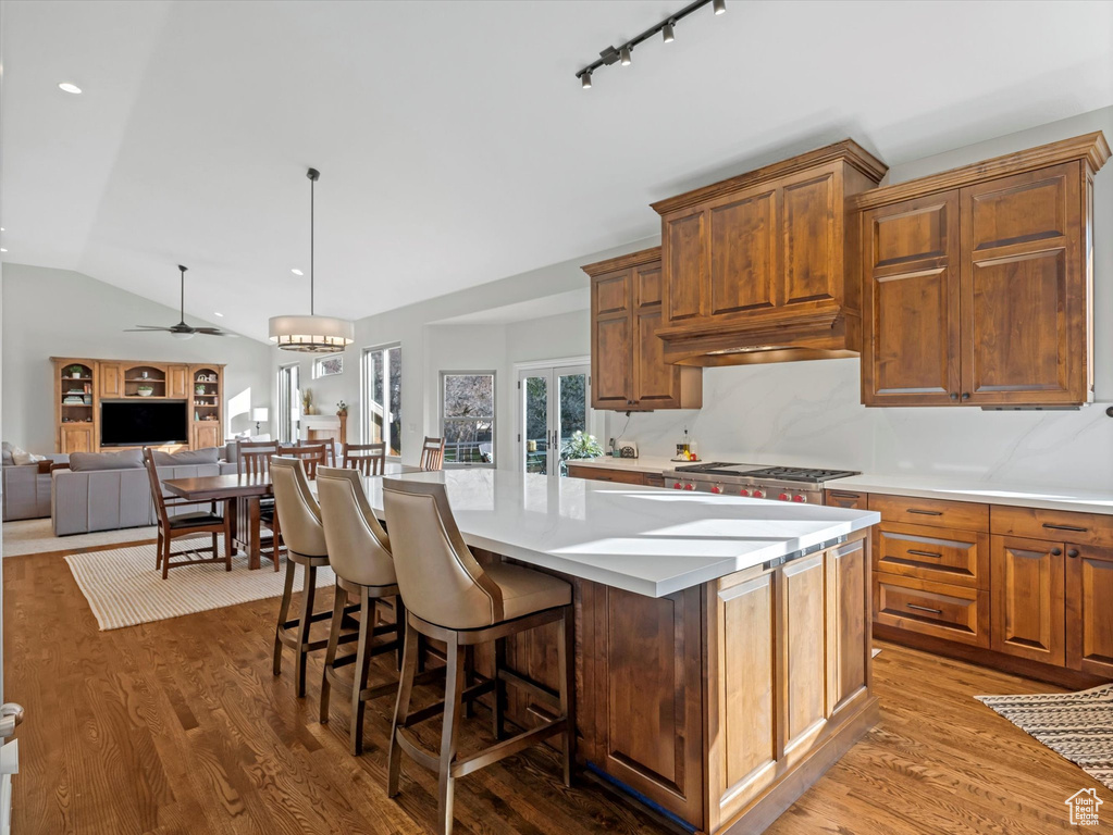 Kitchen featuring vaulted ceiling, a kitchen island, light countertops, wood finished floors, and a ceiling fan
