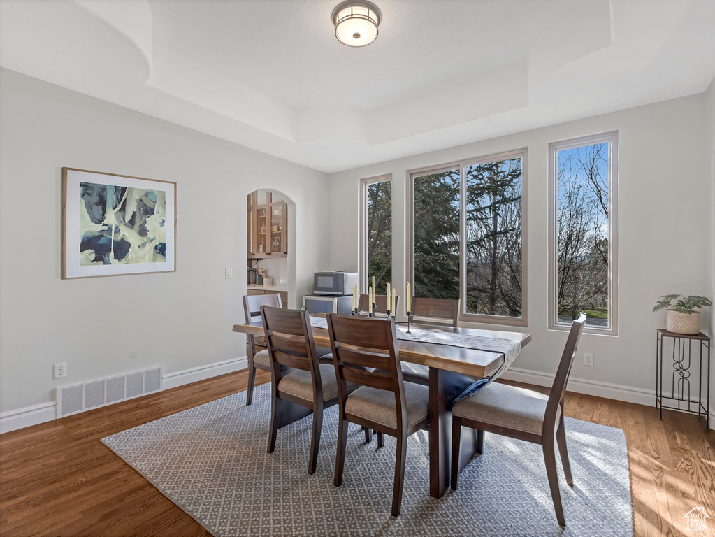 Dining room with a raised ceiling, wood finished floors, and arched walkways