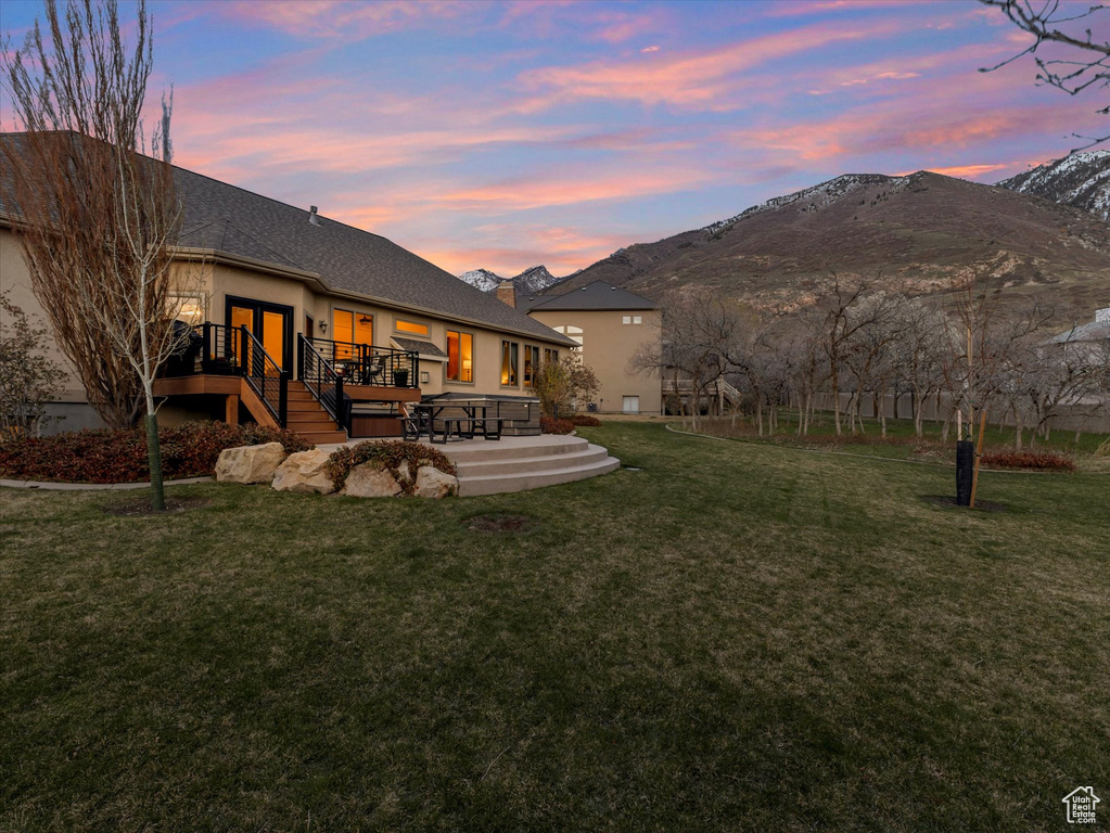 Back of house at dusk with stucco siding, a deck with mountain view, and a lawn