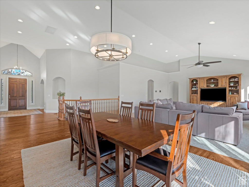 Dining room with arched walkways, a chandelier, wood finished floors, ceiling fan, and high vaulted ceiling