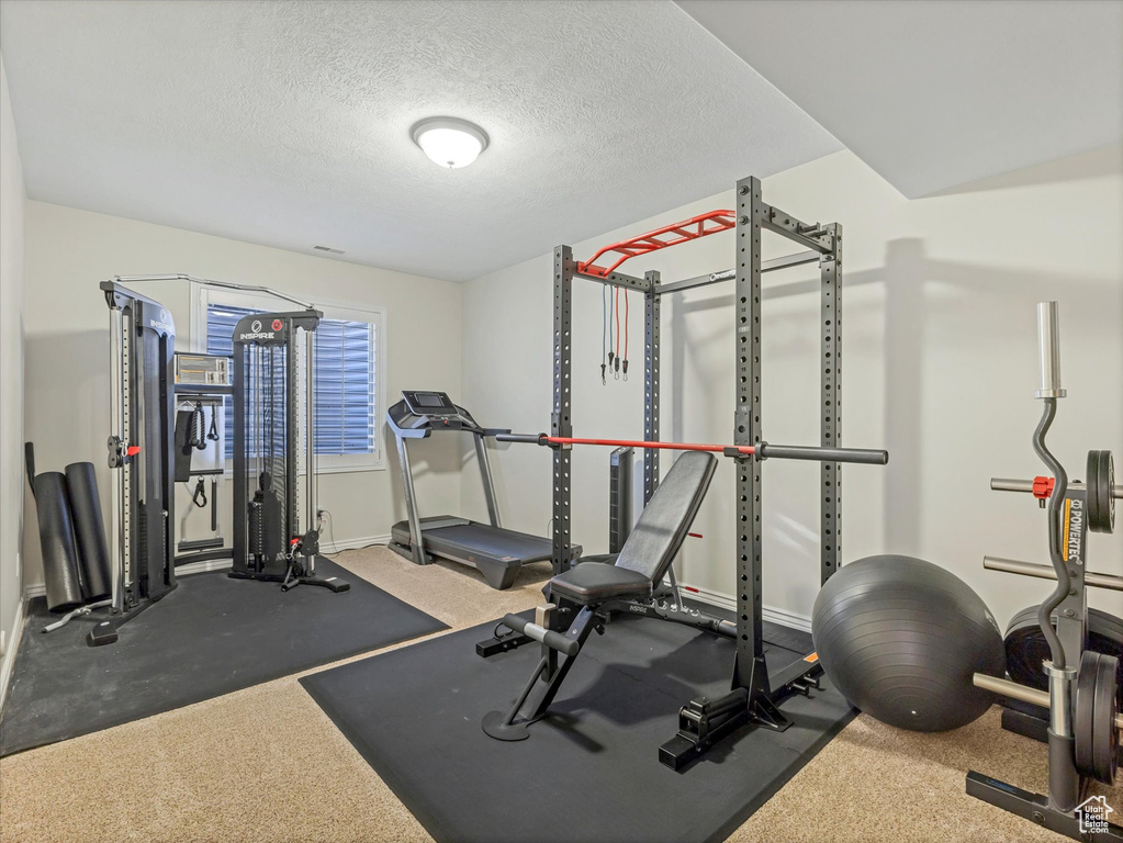 Exercise room featuring baseboards, a textured ceiling, and carpet