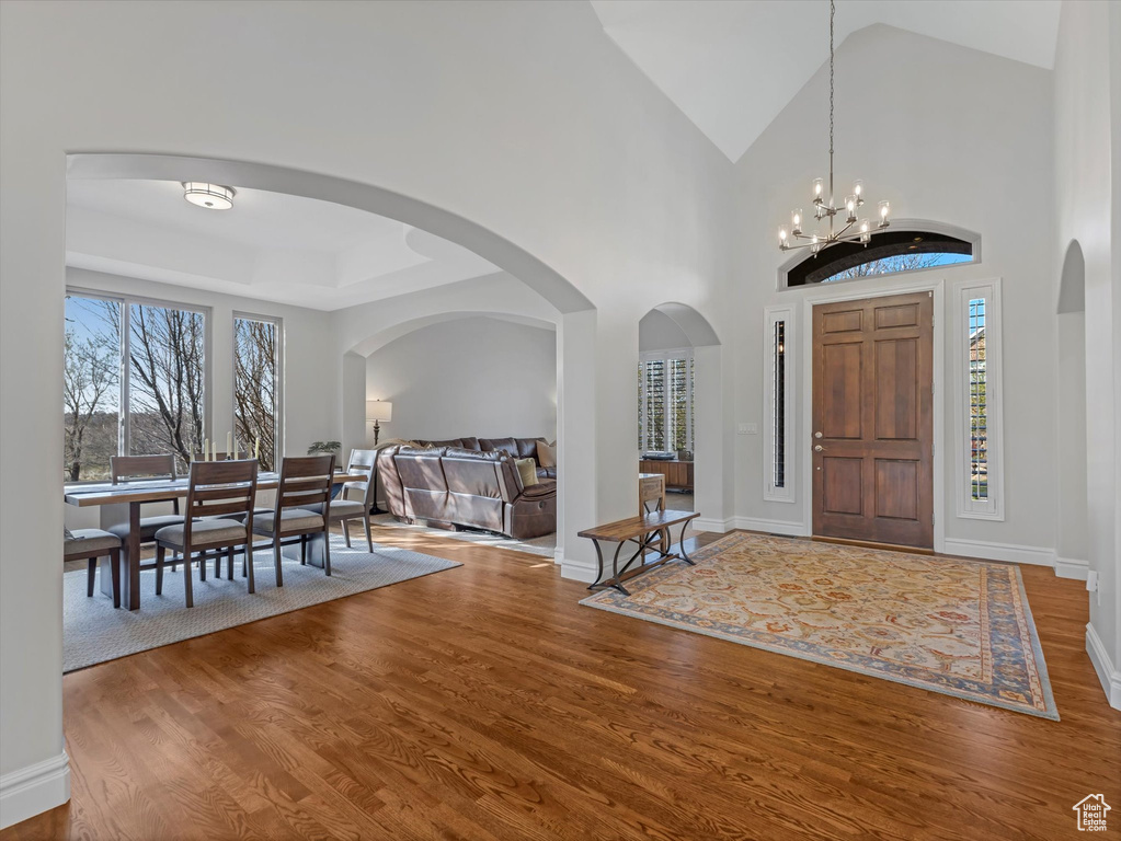 Foyer with wood finished floors, healthy amount of natural light, a chandelier, arched walkways, and vaulted ceiling