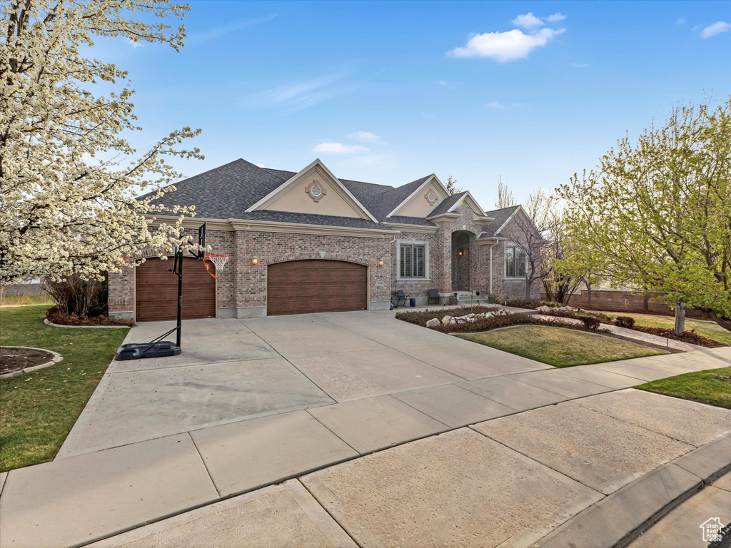 French country inspired facade featuring an attached garage, a front lawn, brick siding, concrete driveway, and roof with shingles
