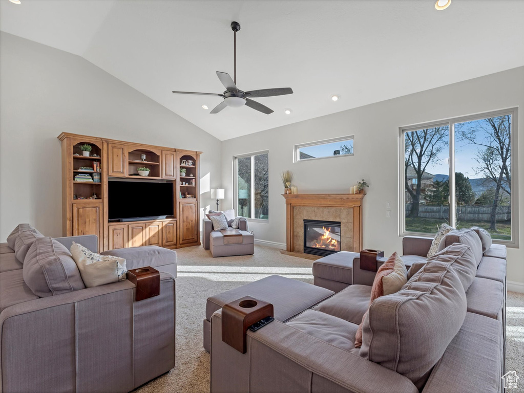 Living room with light colored carpet, a ceiling fan, a tiled fireplace, recessed lighting, and high vaulted ceiling