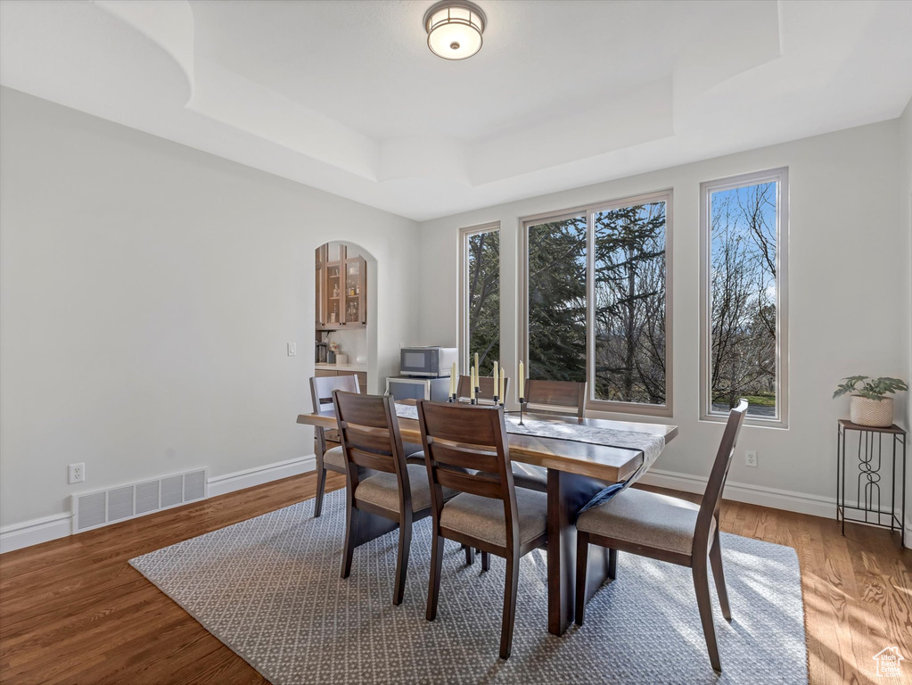 Dining space featuring a raised ceiling, wood finished floors, arched walkways, and baseboards