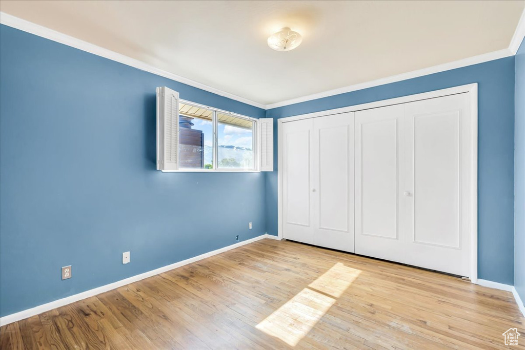 Unfurnished bedroom featuring ornamental molding, baseboards, wood finished floors, and a closet