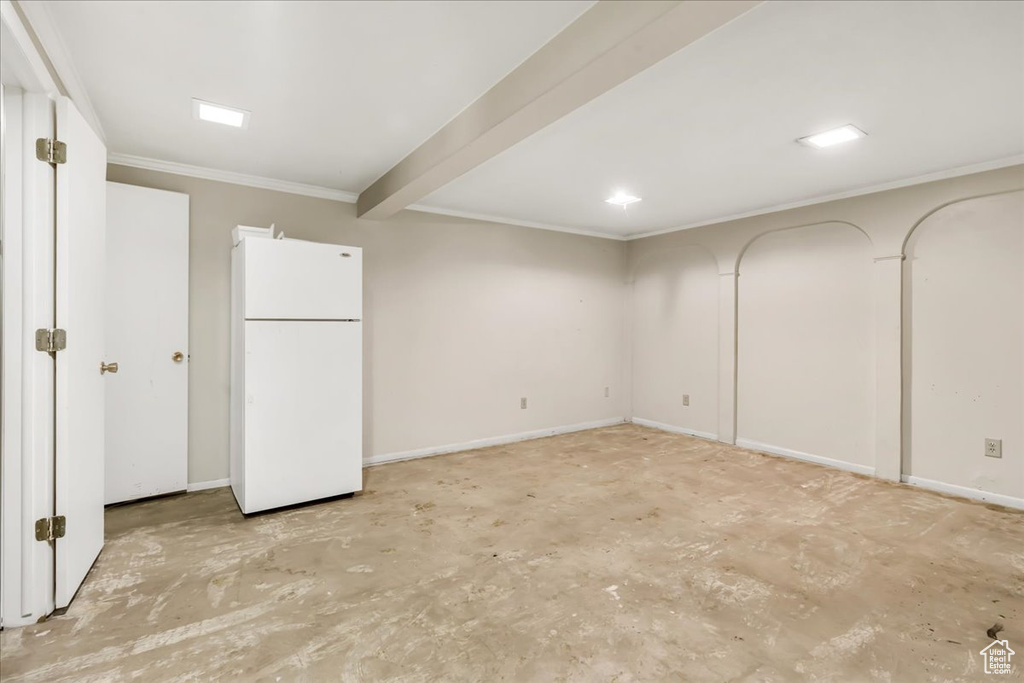 Basement with freestanding refrigerator, crown molding, and baseboards