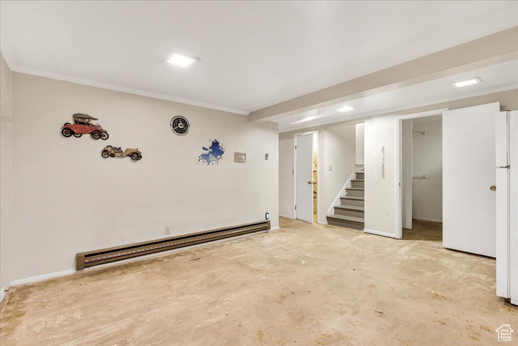 Finished basement featuring a baseboard heating unit, stairway, crown molding, and freestanding refrigerator