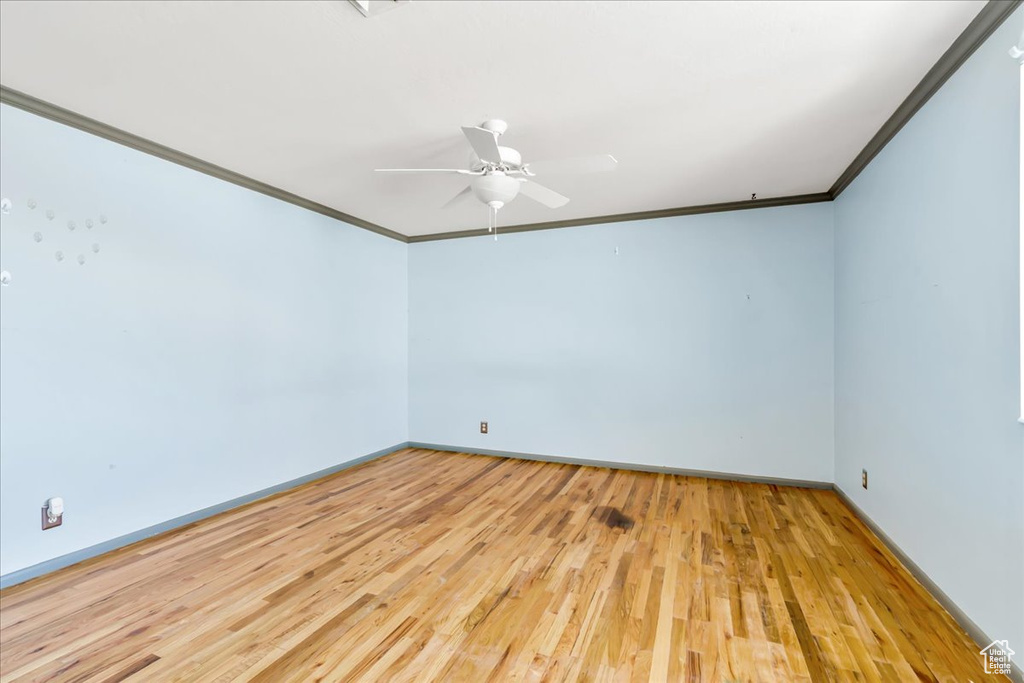 Empty room with crown molding, wood finished floors, baseboards, and a ceiling fan