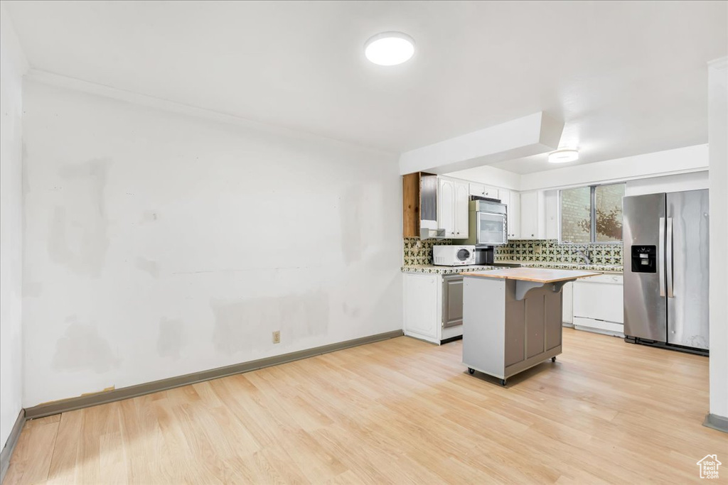 Kitchen with white appliances, light wood-type flooring, backsplash, light countertops, and a breakfast bar