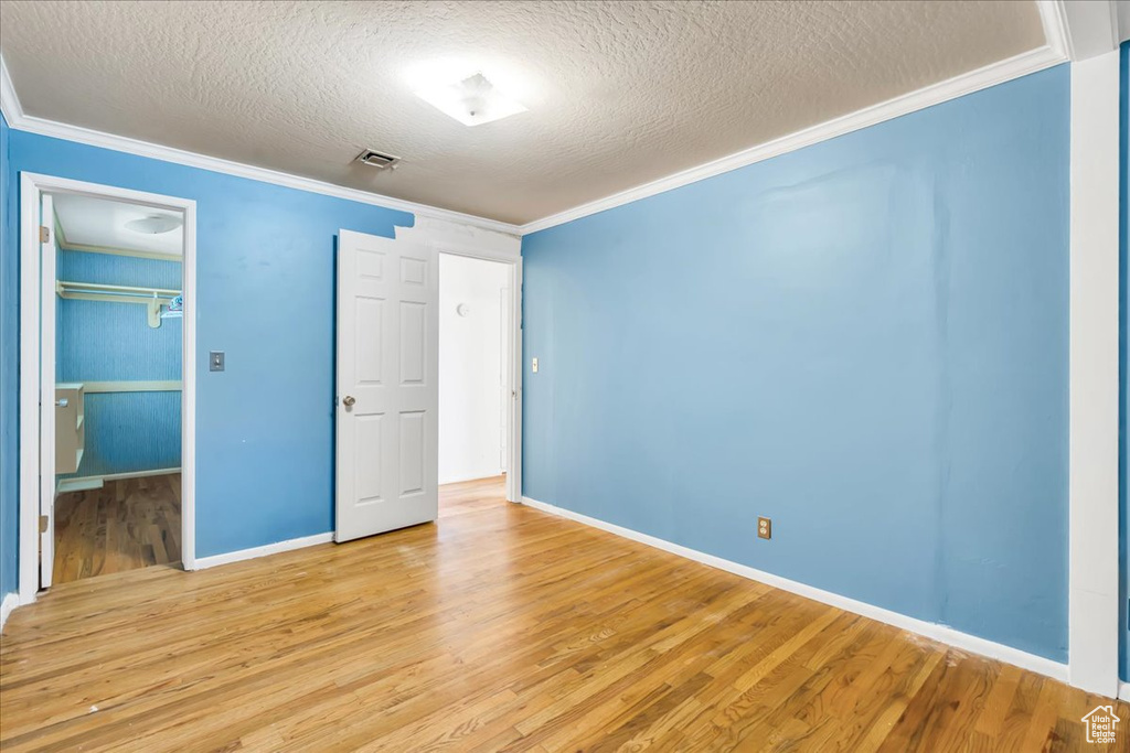 Unfurnished bedroom featuring ornamental molding, a textured ceiling, light wood-style floors, a walk in closet, and baseboards