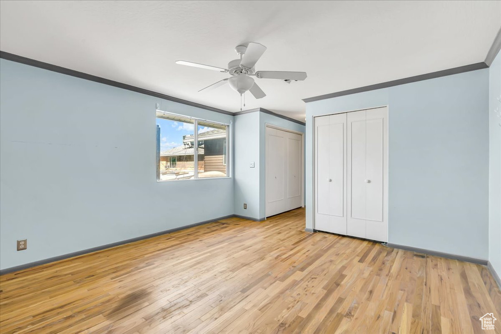Unfurnished bedroom featuring ornamental molding, light wood-style flooring, multiple closets, baseboards, and a ceiling fan