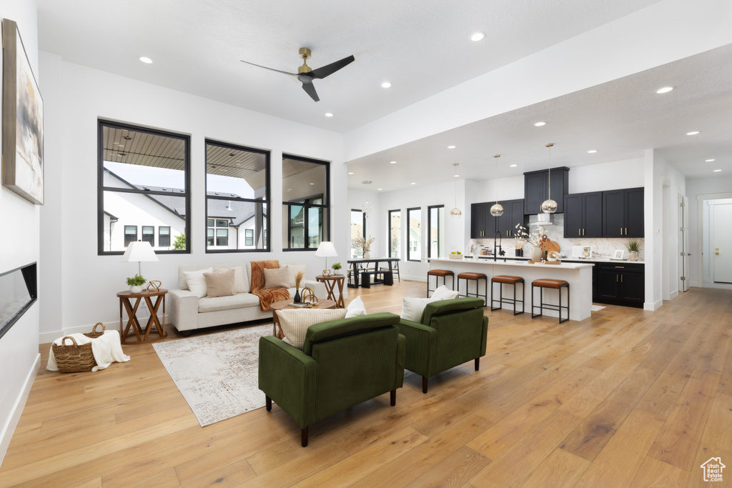 Living room with light wood-type flooring, a ceiling fan, recessed lighting, a glass covered fireplace, and baseboards