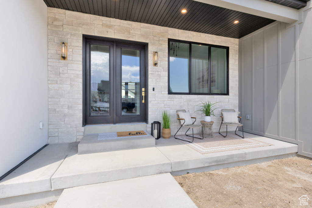 Entrance to property with board and batten siding, stone siding, and french doors