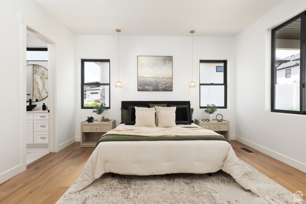 Bedroom with light wood-type flooring, multiple windows, baseboards, and ensuite bathroom