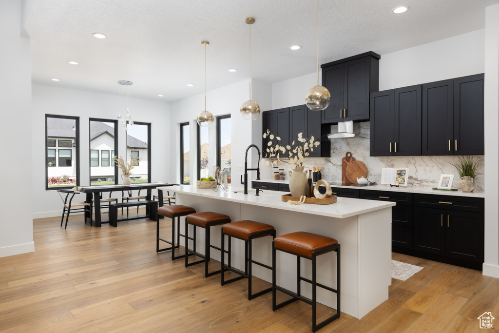 Kitchen with wall chimney exhaust hood, light countertops, backsplash, a kitchen bar, and recessed lighting