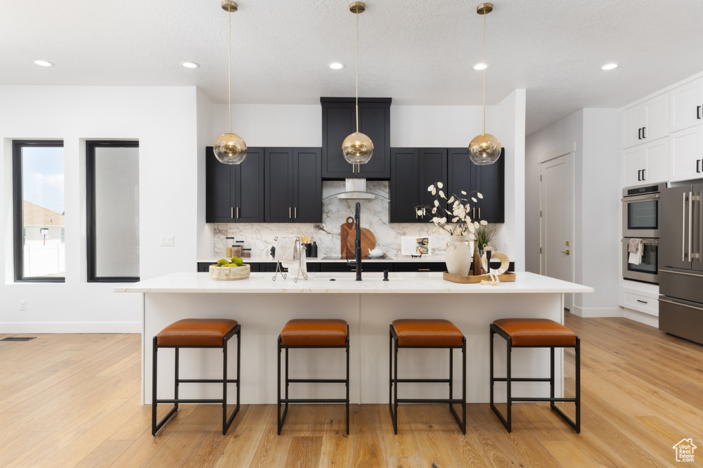 Kitchen featuring stainless steel appliances, a kitchen breakfast bar, decorative backsplash, light countertops, and recessed lighting