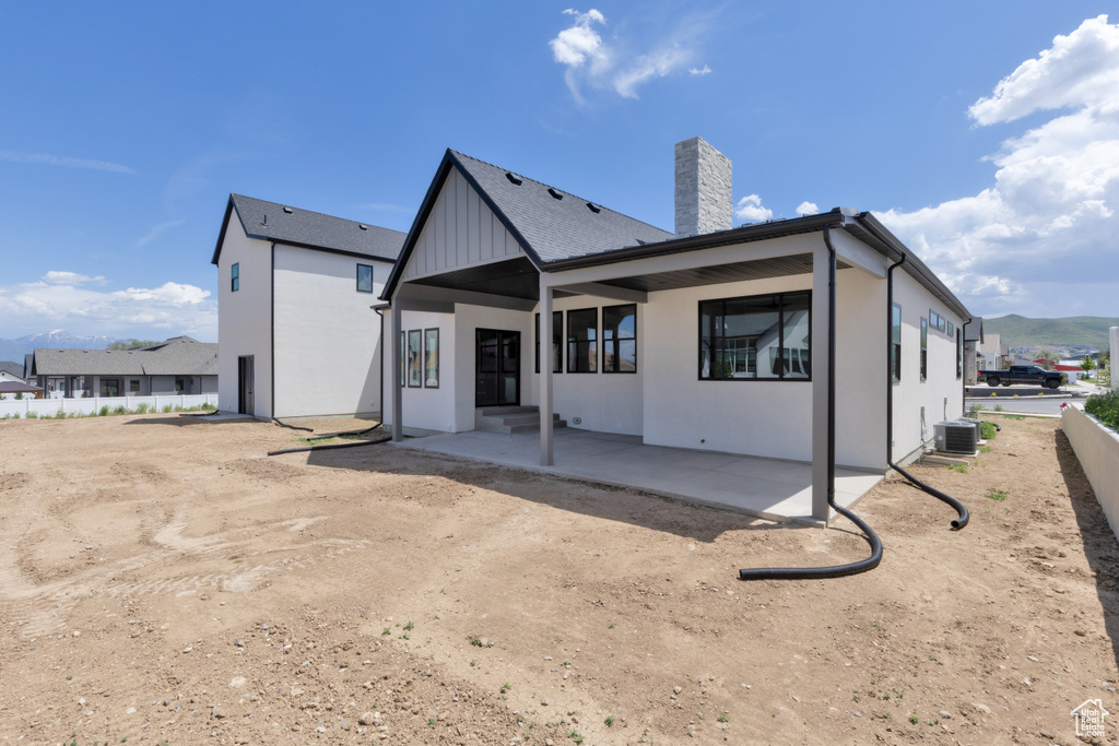 Back of property with a chimney, a patio area, central air condition unit, and board and batten siding