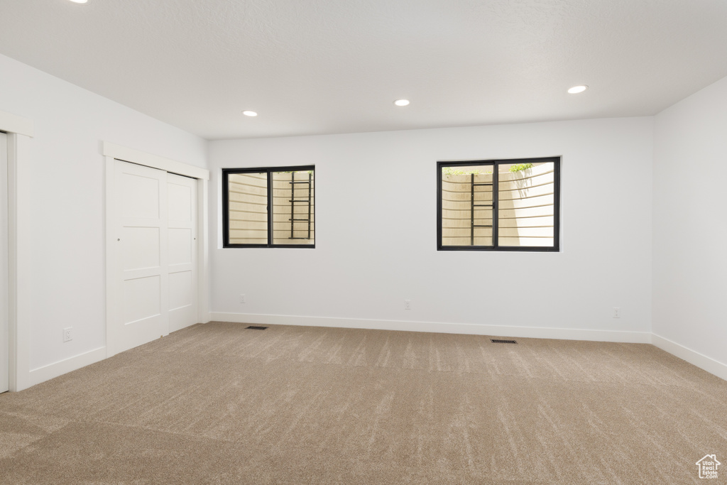 Unfurnished bedroom featuring light colored carpet, multiple windows, baseboards, and recessed lighting