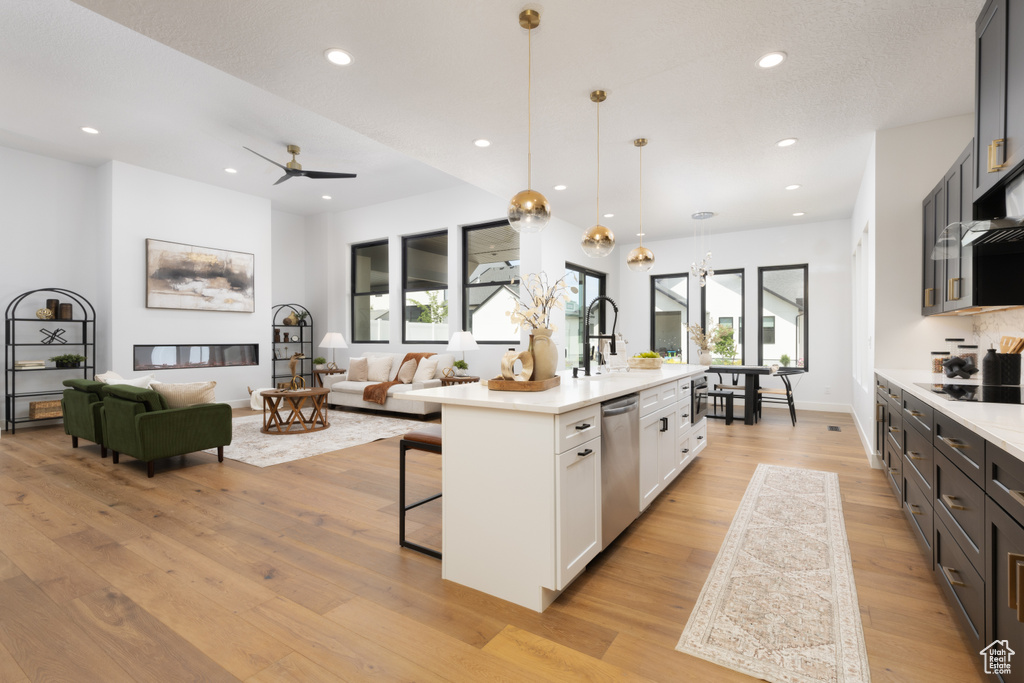 Kitchen featuring light countertops, light wood-type flooring, stainless steel dishwasher, a kitchen breakfast bar, and black electric stovetop