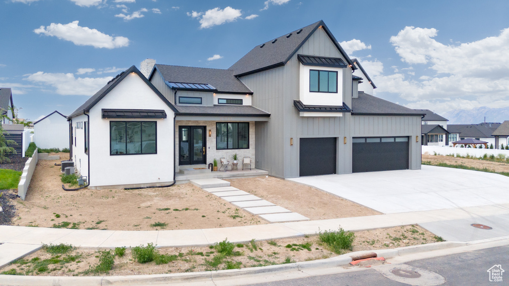 Modern farmhouse featuring a standing seam roof, driveway, an attached garage, metal roof, and board and batten siding