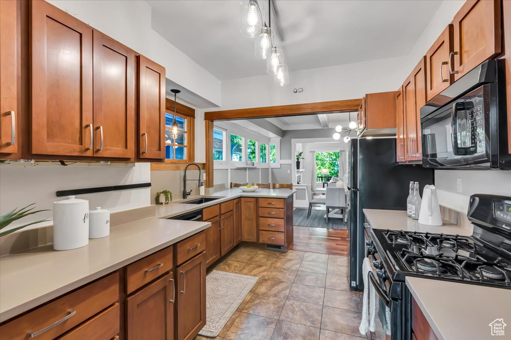 Kitchen featuring black appliances, a sink, light countertops, a peninsula, and brown cabinetry