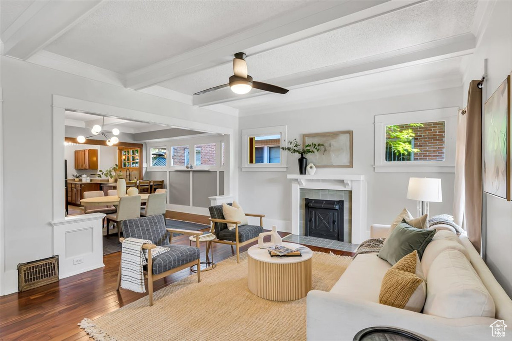 Living area featuring beam ceiling, a tiled fireplace, wood finished floors, healthy amount of natural light, and a chandelier