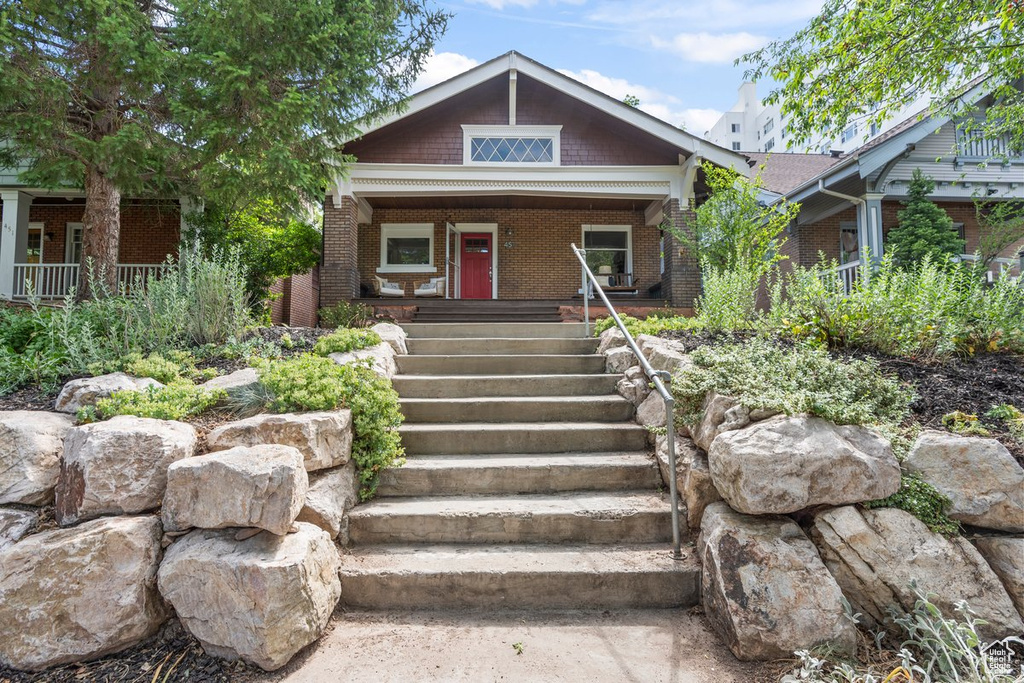 View of front of house with a porch, brick siding, and stairway