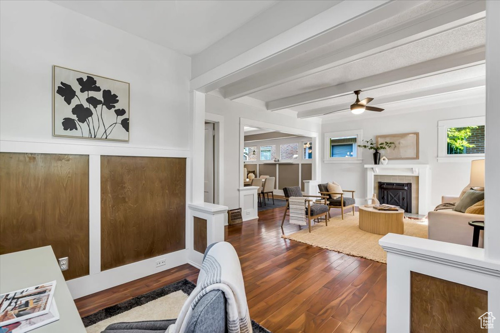 Living area with dark wood-type flooring, a fireplace, beamed ceiling, and a ceiling fan