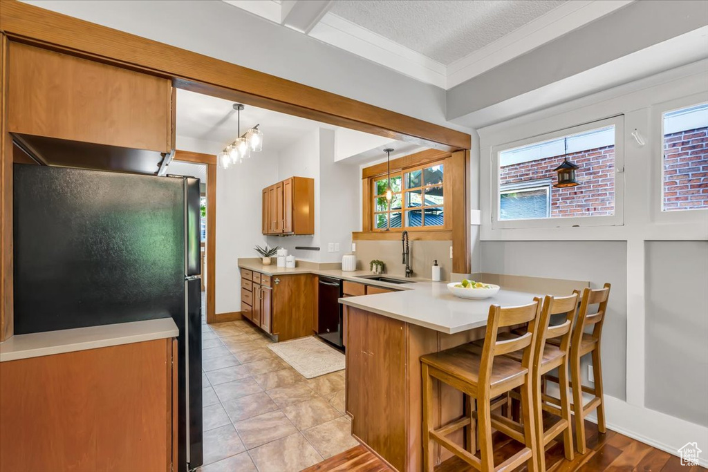 Kitchen featuring a sink, black appliances, a peninsula, brown cabinets, and light countertops
