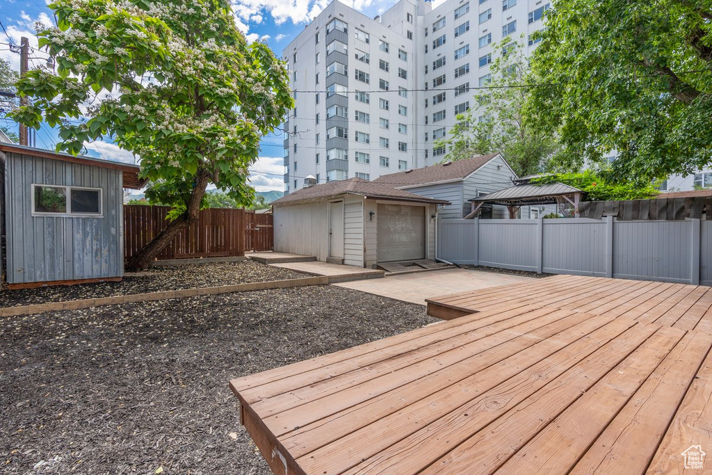 Wooden terrace featuring a fenced backyard, an outbuilding, a garage, and a gazebo