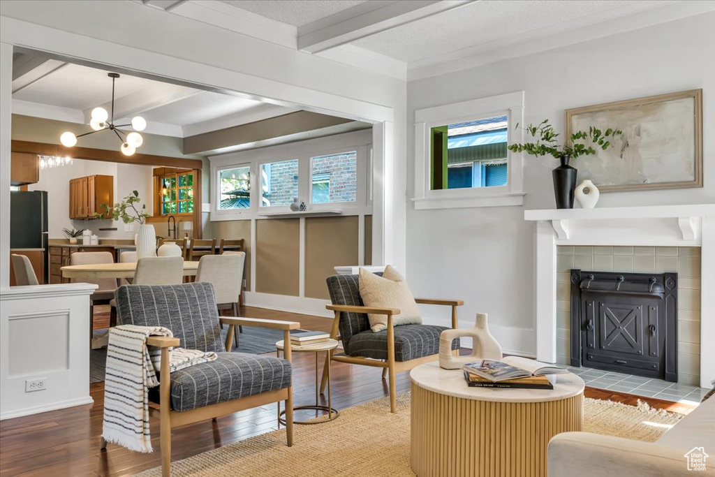 Living area with beamed ceiling, a tiled fireplace, light wood-style flooring, and a chandelier